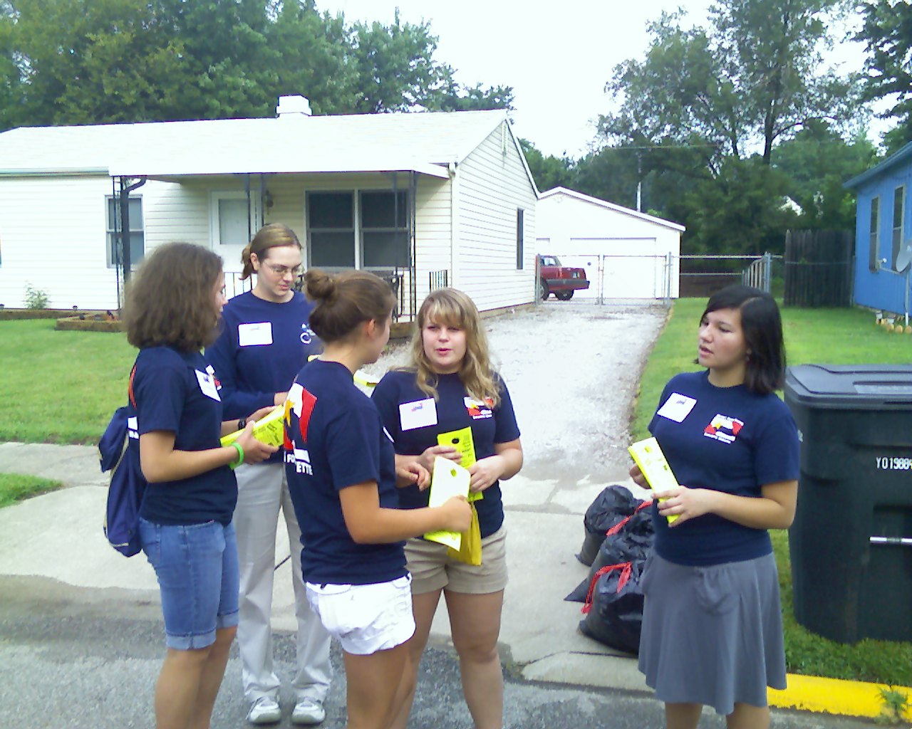 Young girls standing outside a home in front of a recycling bin